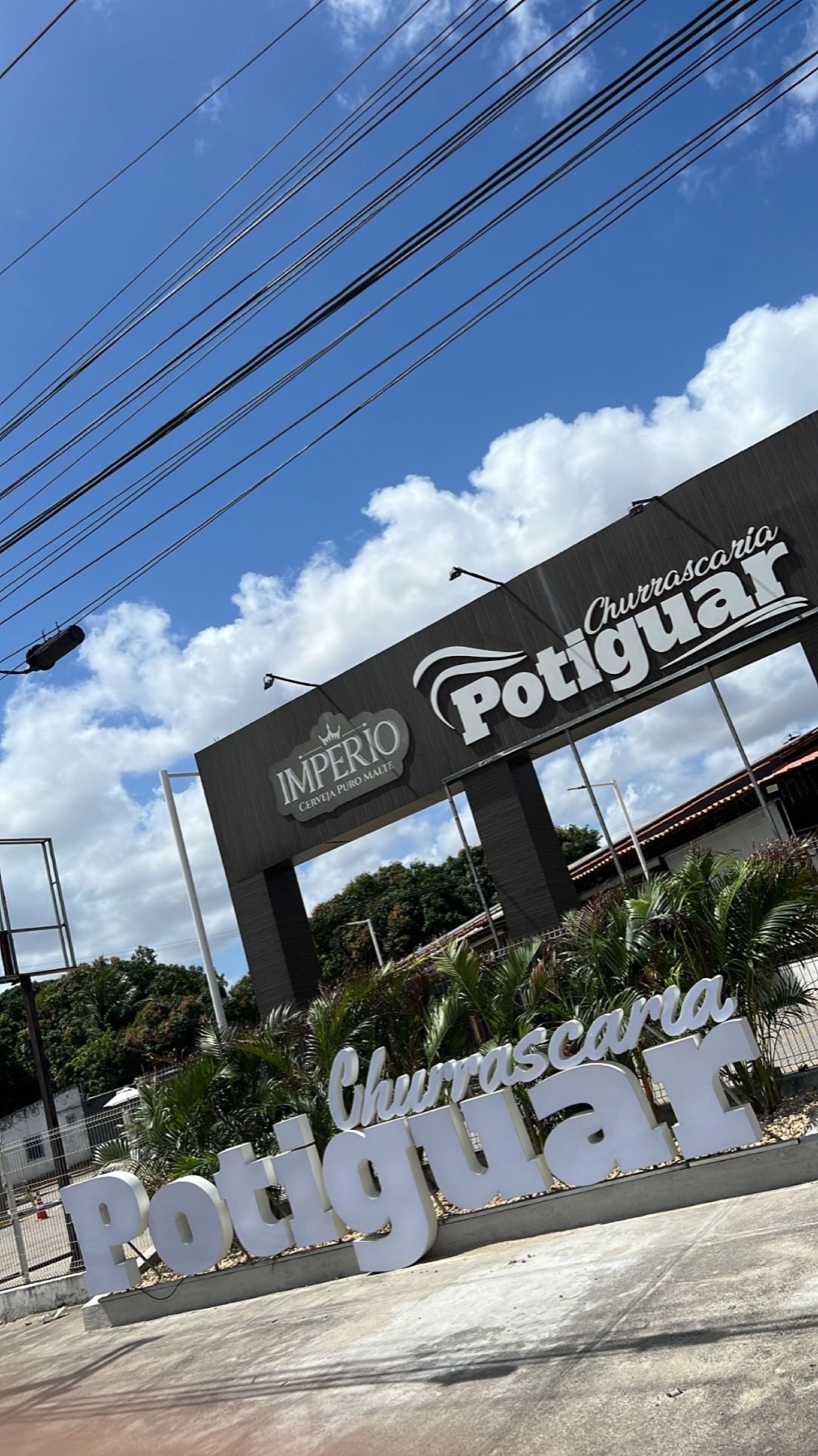 Entrada da Churrascaria Potiguar no Eusébio: letreiro grande entre plantas e pórtico de madeira sob céu azul
