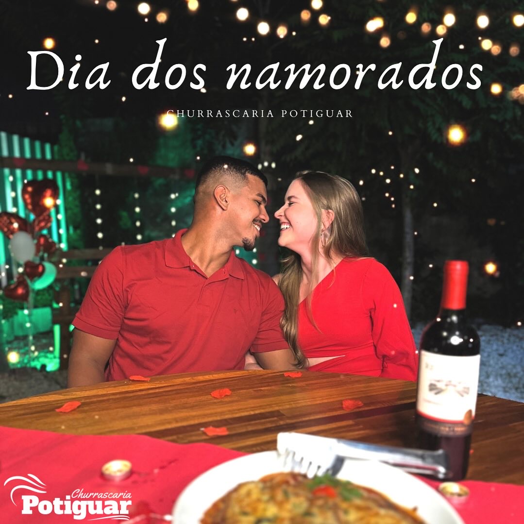 Casal sorrindo à mesa de madeira sob varal de luzes, em publicação de Dia dos Namorados do perfil oficial