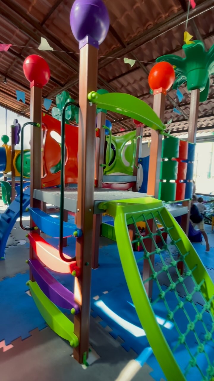 Parquinho infantil colorido e coberto, com crianças ao fundo, registrado no perfil oficial